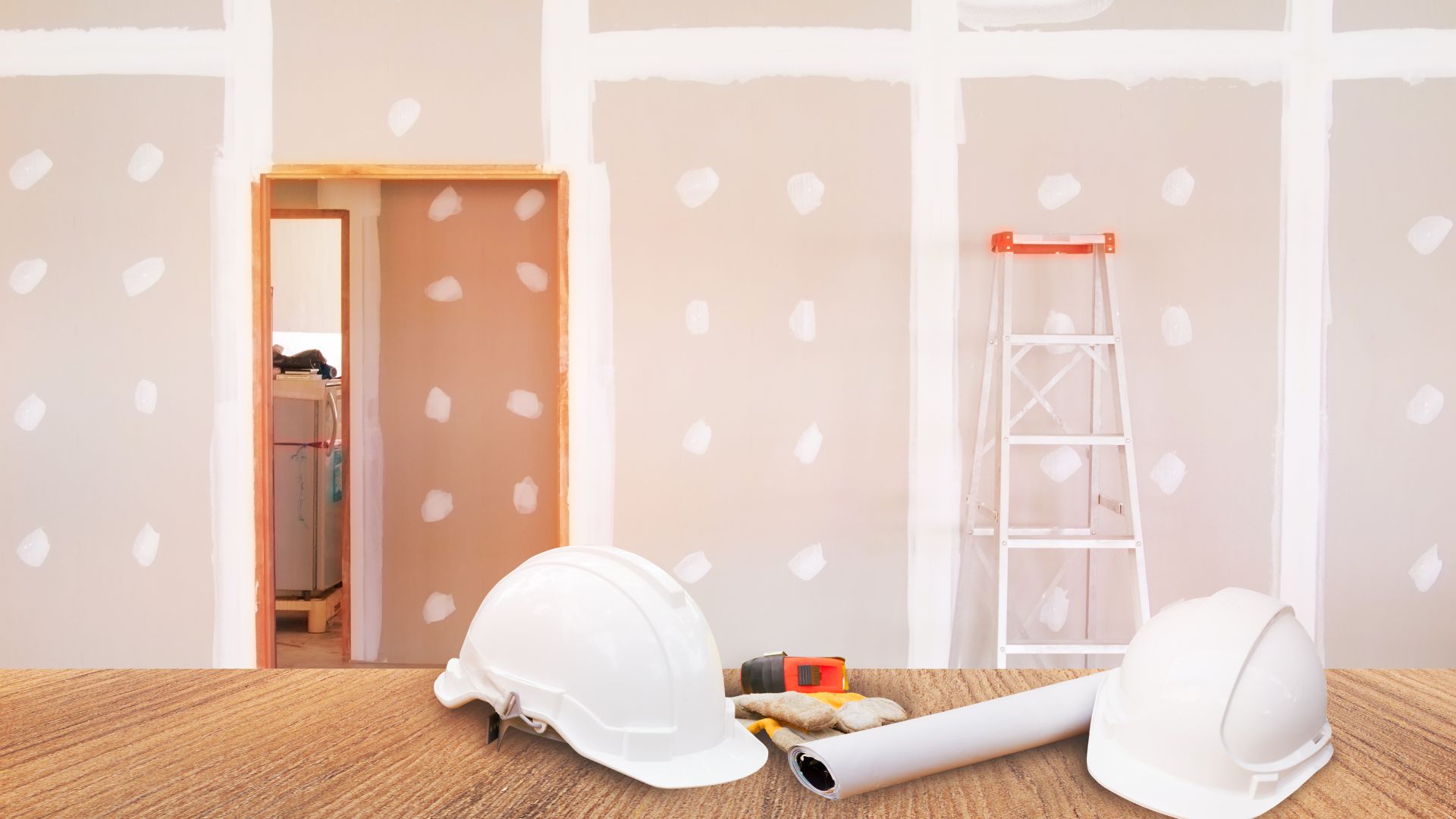 A room with a ladder, hard hat, and paint rollers